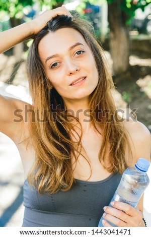 Young woman with a bottle of water after Jogging outdoors in Singapore. She is wearing grey top and a light sports leggings