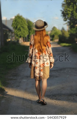 A young girl with long hair in a hat walking down the village street. The girl's hair in the sunlight.