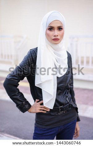 Fashionable female model in blue jeans, long sleeves black leather jacket with hijab posing in urban environments. Stylish Muslim female hijab fashion lifestyle portraiture concept.