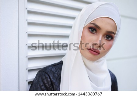 Fashionable female model in blue jeans, long sleeves black leather jacket with hijab posing in urban environments. Stylish Muslim female hijab fashion lifestyle portraiture concept.