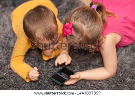 Little children watching cartoon on a smartphone while lying on the carpet in a room at home