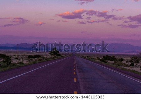 image of an empty road ending in mountains with a purple sunset