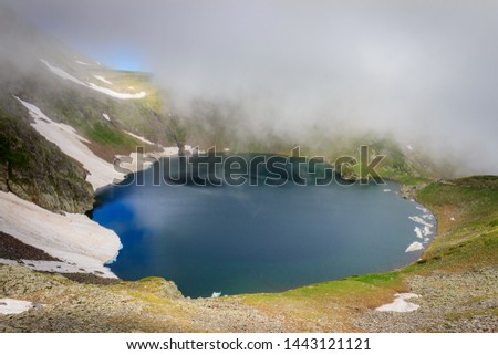 Beautiful misty view of famous the Eye lake on Rila mountain in Bulgaria, sunlit landscape and lots of mountain hikers walking on the highlands