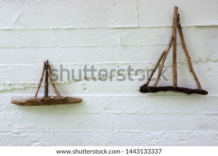 Two handcrafted wooden small boats made from twigs of driftwood as decoration on a white painted concrete wall in a Greek island at summer holidays