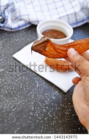 Close-up of a person dipping and eating a churro ringlet in a chocolate sauce - concept with churro kringle and dip on dark marble background with a dishcloth