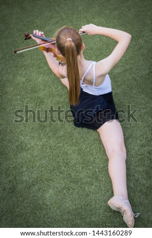 girl in spagat ballet pose playing the violin on green grass placed diagonally in the picture