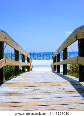 Perspective photography of wooden boardwalk walkover bridge to beach with turquoise blue ocean water on horizon.