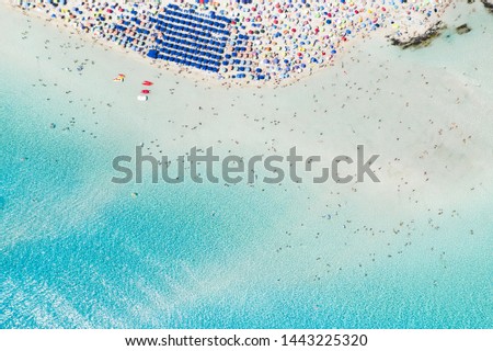 Stunning aerial view of the Spiaggia Della Pelosa (Pelosa Beach) full of colored beach umbrellas and people sunbathing and swimming in a beautiful turquoise clear water. Stintino, Sardinia, Italy. Royalty-Free Stock Photo #1443225320