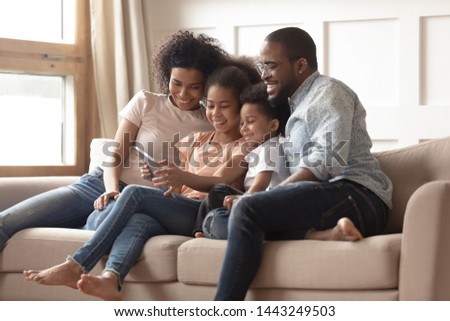 Happy young black family with preschooler children have fun relax together on sofa at home watching video on tablet, smiling parents enjoy spending time with little kids rest on couch using pad