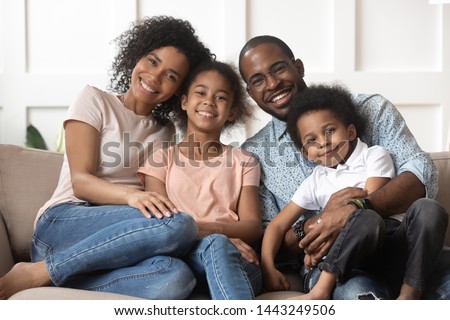 Portrait of happy young african American family with little kids sit relax on couch cuddling, smiling black parents rest on sofa hug preschooler children posing for picture at home together Royalty-Free Stock Photo #1443249506