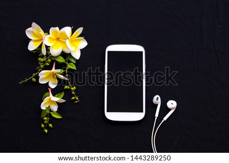 mobile phone ,earphone and yellow flowers frangipani arrangement flat lay style on background black