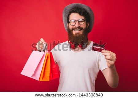 It&#039;s shopping time ! Photo of stylish bearded guy shopping with new credit card, over red background 