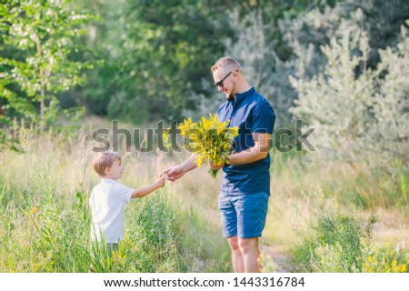 Little boy with his father collect summer flowers on the meadow. Horizontal photo