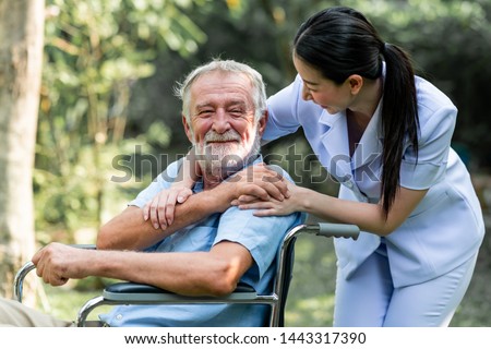 Caring nurse with senior man sitting on wheelchair in gaden. Asian woman, caucasian man. Happy laugh. Royalty-Free Stock Photo #1443317390
