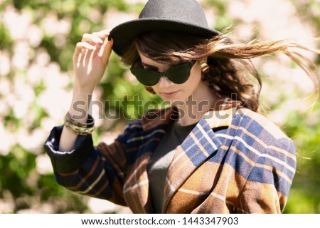 A portrait of a young fashionable woman in sunglasses and a hat walking in the park. Beauty, fashion, optics.