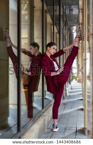 a young european girl with a short haircut brunette summer day shows stretching near the glass wall of a business center. The gymnast trains in the urban environment and does the splits. Women's suit