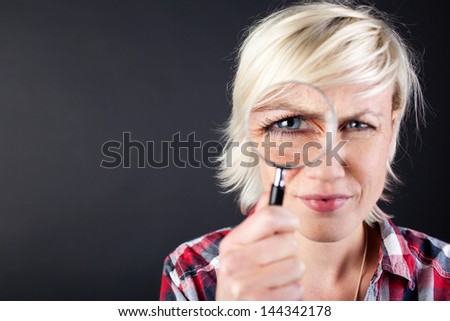 Closeup portrait of a young woman with magnifying glass against black background