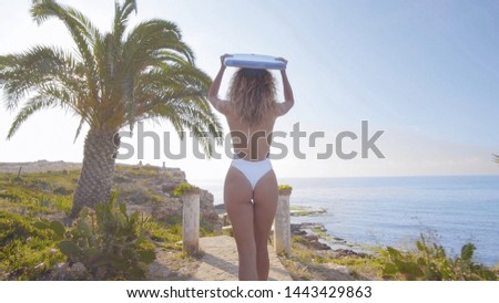 Beautiful young woman surfer walking down beach at sunset.