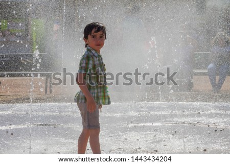 Cute little boy is laughing and having fun running under a water fountain
