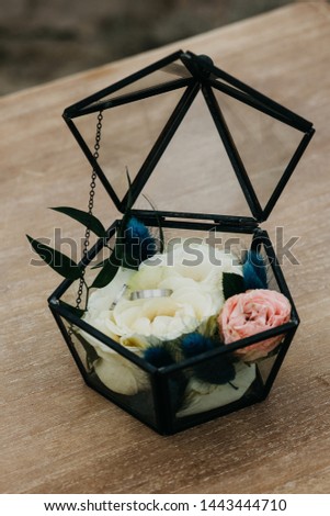 Closeup wedding rings in white gold or platinum in a transparent box with a white rose. Traditional details of a wedding event.