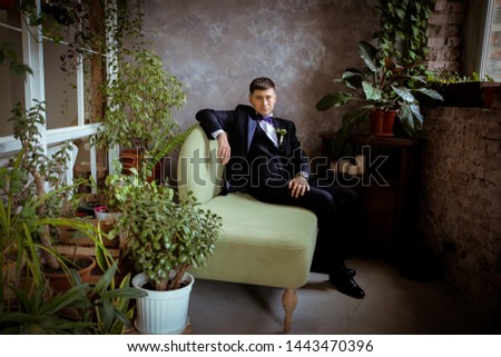 Sad groom without a bride is sitting on the green sofa