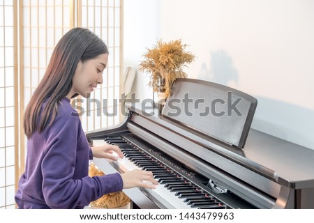 Cheerful Smiling asian young girl playing piano in sost light. Beautiful,happy, joyful, relaxing woman practising piano cheerfully. 