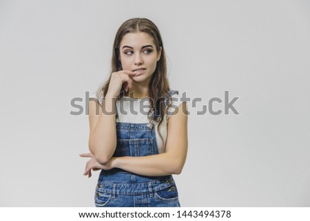 Sweet beautiful blond woman with very long hair in blue jeans overalls and glasses over grey background