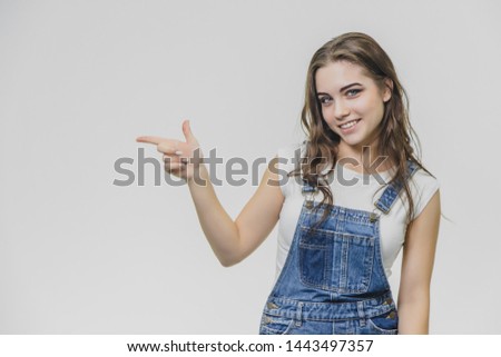 Happy young blond woman in jeans overalls and glasses over grey background