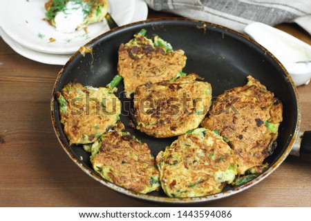 Proper nutrition, vegetarian breakfast gluten free,zucchini courgette pancakes with beans, mint on frying pan with sour greek yogurt, black background, towel, fork, knife on wooden surface