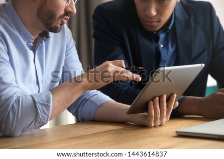 Diverse businessmen talking using digital tablet sit at office desk, male team two men working looking at tech device touchpad screen, corporate technology business apps concept, close up view Royalty-Free Stock Photo #1443614837