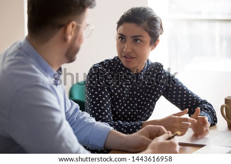 Young indian female mentor coach worker talking to male coworker teaching intern having business conversation with workmate, serious hindu manager helping colleague discussing new project in office Royalty-Free Stock Photo #1443616958