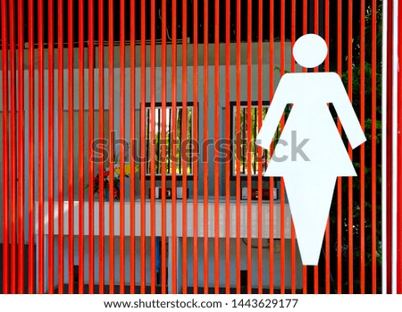 A large white female toilet sign on the red cage wall