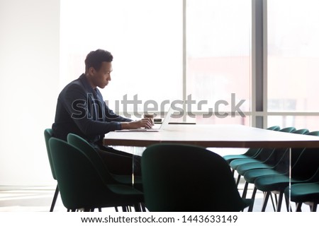 Focused african american businessman in suit working on computer sit at conference table in modern office, serious black executive using laptop prepare for business meeting in boardroom interior