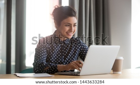 Happy young indian business woman entrepreneur using computer looking at screen working in internet sit at office desk, smiling hindu female professional employee typing email on laptop at workplace Royalty-Free Stock Photo #1443633284
