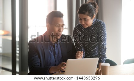 Indian and african colleagues talk at workplace, professional mentor teacher help black intern explain computer work, two serious diverse coworkers discuss online project teamwork mentoring in office Royalty-Free Stock Photo #1443633296