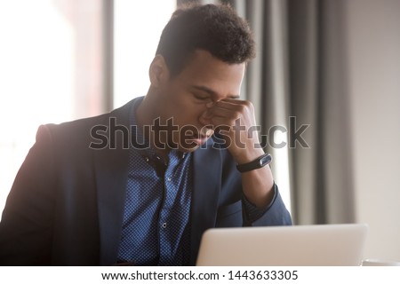 Frustrated stressed black businessman feel eye strain headache tired after office work computer use, exhausted upset african man sit at desk suffer from overwork blurry vision problem fatigue concept Royalty-Free Stock Photo #1443633305