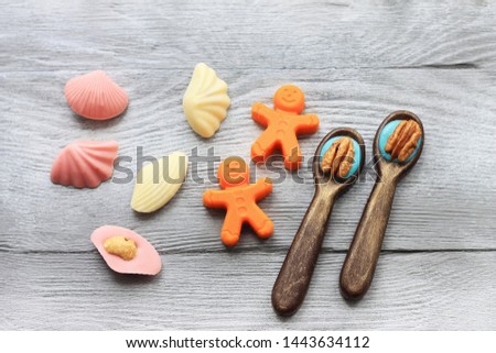 Little chocolate figures. Spoons, little men, shells on light wooden background. Sweet art and food.