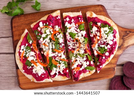 Beet hummus flat bread with feta cheese. Top view on a paddle board against a wood background. Healthy eating concept. 