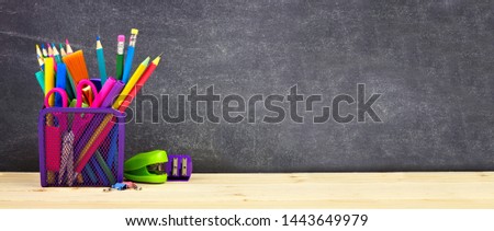 School supplies on a wood desk with chalkboard background. Side view. Back to school concept. Copy space. Banner orientation.