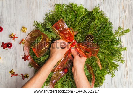 Florist makes a Christmas wreath of fir branches. Top view of female hands. Flat lay. Ribbon decoration. Royalty-Free Stock Photo #1443652217