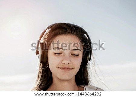 Close-up portrait of young girl's head in big headphones, blue bright sky background