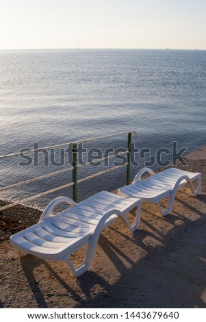 Two plastic white sunlongers on the stone pier on the sea Royalty-Free Stock Photo #1443679640