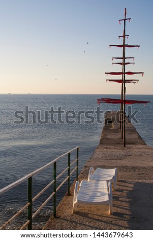 Two plastic white sunlongers on the stone pier on the sea Royalty-Free Stock Photo #1443679643