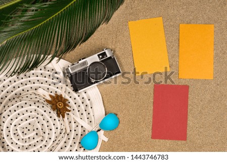 Vacation, travel and summer concept - notebook with palm leave, hat and vintage photo cameraon beach sand