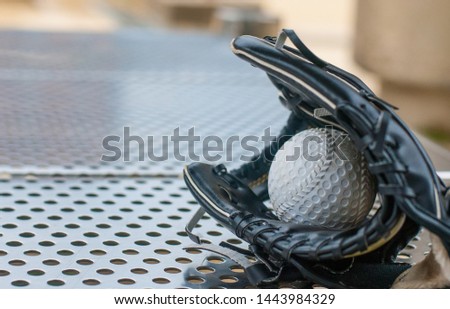 Black bestball glove holding a white baseball and placed on the stainless steel bench, with soft tone