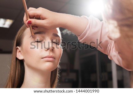 makeup artist appling a primer on an eyelid of a young beautiful client using a brush before dabbing eyeshadows. concept of professional make up training Royalty-Free Stock Photo #1444001990