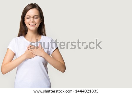 Headshot of happy woman feeling blessed with eyes closed. Studio portrait of young female teenager expressing harmony, peace, calmness isolated on gray background. People emotions concept, copy space