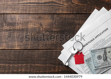 mortgage application. Key with red keychain house and blank and money on a brown wooden table. concept of buying a home. top view