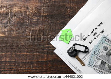 new home purchase and sale agreement. Key with keyring and blank and money on a brown wooden table. concept of buying a home. top view