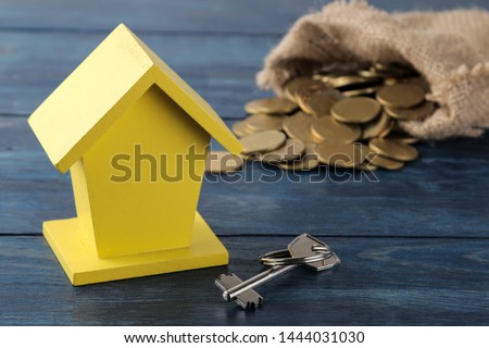 Key and yellow decorative house and money in the background on a blue wooden table. home buying concept